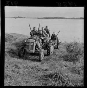 Unidentified hunters leave a lake in a tractor covered in dead game at the opening of the duck shooting season, including guns and tussock