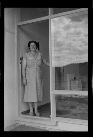 Unidentified woman standing at the glass door of her house, Kawerau