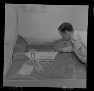 An unidentified man with a model of a hydro-electric dam, at Diamond Jubilee Exhibition, industrial fair, Petone, Lower Hutt City