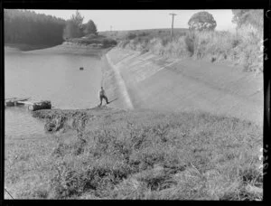 Unidentified man, with a little dog, showing the low level of water in a reservoir, during a water shortage, Marton, Rangitikei District