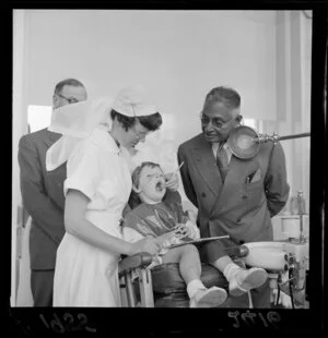Sir John Kotelawala, Prime Minister of Ceylon, at the New Zealand Dental School, Wellington, with dental nurse and child