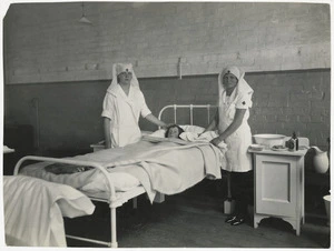 Red Cross nurses with a patient in a hospital bed, location unidentified