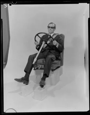 Man in studio sitting in car seat, with steering wheel and seatbelt