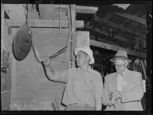 Worker striking a gong at sheep shearing, Ohinewairua Station