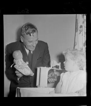 Lower Hutt Mayor Percy Dowse weighs toddler Angela White whilst distracting her with a doll