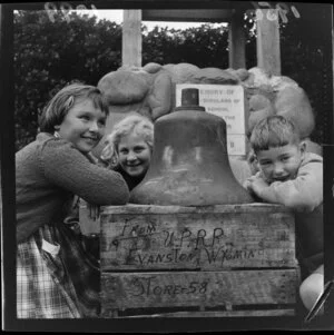 Island Bay School pupils with a large bell that rests on a wooden crate, which has written on the side 'From Union Pacific Railroad, Evanston, Wyoming, United States'