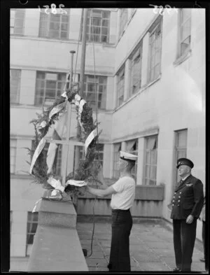 An unidentified navy cadet hoisting a garland to the masthead of the HMNZS Wakefield, Stout Street, Wellington