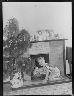 Preparing for Christmas, boy beside Christmas tree with note for Santa above fireplace