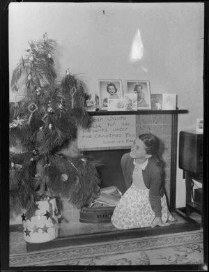 Preparing for Christmas, girl beside Christmas tree with note for Santa above fireplace