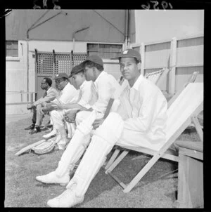 West Indian cricket team members wait their turn to bat during a match between Wellington and the West Indies at the Basin Reserve, including caps, bats, pads and deck chairs