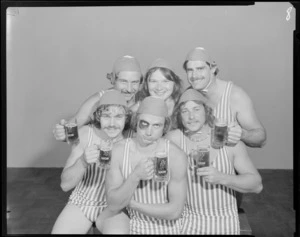 People (one with a fake black eye) in surf lifesaving costumes, drinking Lion beer in studio