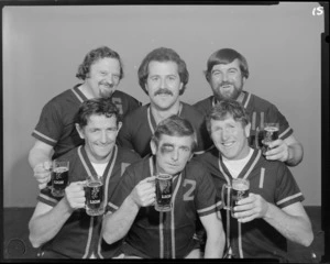 People (including one with fake black eye) in softball uniforms drinking Lion beer in studio