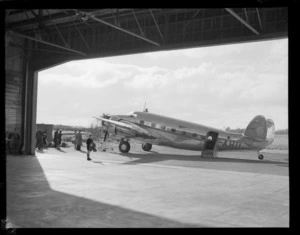 Lockheed Lodestar aeroplane ZK-AHU, standing outside a hangar, with unidentified group of people with suitcases alongside, location unidentified