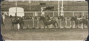 Three jockeys ride horses past spectators on the racecourse