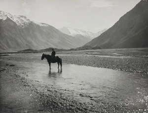 Horse rider stands in South Island braided river valley