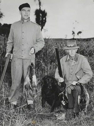 Two game hunters pose with pheasant birds and dog