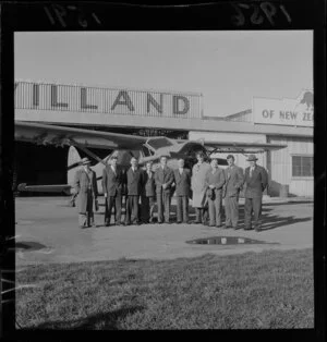 Sir Edmund Hillary and a group of unidentified men in front of an airplane, Rongotai Airport, Wellington