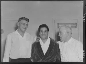 Italian/Australian boxer Luigi Coluzzi in a robe in his dressing rooms with two unidentified men [trainer?] before a boxing match against Billy Beazley, Wellington Town Hall