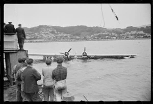 Men watching a Royal New Zealand Air Force Catalina flying boat on cable in water, Evans Bay, Wellington