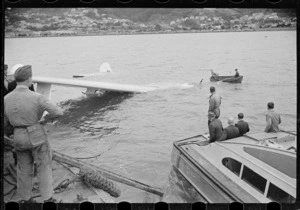 Men on floating crane watching a Royal New Zealand Air Force Catalina flying boat being raised from sea, Evans Bay, Wellington