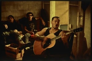 Production still of Jake Heke playing the guitar and singing at a party