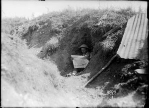 A New Zealand soldier reading a newspaper in a captured German trench, France