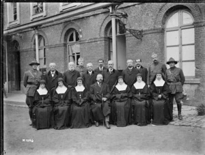 Group portrait of World War I soldiers and civilians, including nuns, outside a brick building