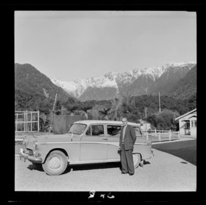 George Groufsky [Maitlands representative of Hokitika?] standing in front of his car with bush in the background at Fox Glacier, West Coast Region