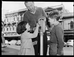 Mr M J Nathan demonstrating parking meter to his children, Lambton Quay, Wellington