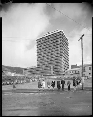 Group at bus stop, outside the Ministry of Works and Development building, Vogel House, Thorndon, Wellington