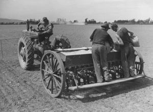 Machinery for sowing seeds, south Canterbury; shows a tractor attached to a driller, and men loading seeds