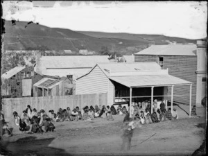 Group of people sitting in a line outside a shop in the Wanganui area, possibly waiting for a land court hearing