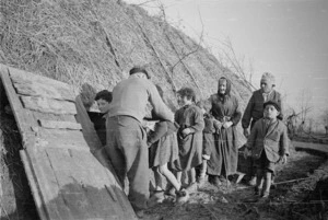New Zealand soldier E Hine, helping Italian refugees into their air-raid shelter underneath a haystack near Faenza, Italy, during World War II - Photograph taken by George Frederick Kaye