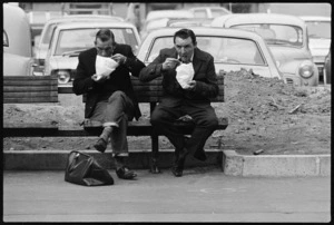 Two men sitting on a bench eating noodles