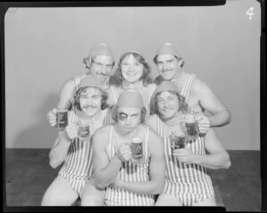 People (one with a fake black eye) in surf lifesaving costumes, drinking Lion beer in studio