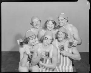 People (one with a fake black eye) in surf lifesaving costumes, drinking Lion beer in studio