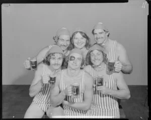 People (one with a fake black eye) in surf lifesaving costumes, drinking Lion beer in studio