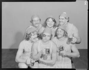 People (one with a fake black eye) in surf lifesaving costumes, drinking Lion beer in studio