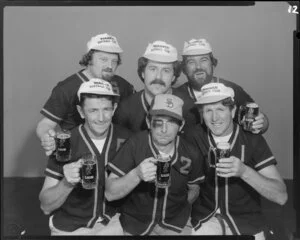 People (including one with fake black eye) in softball uniforms drinking Lion beer in studio