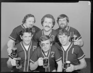 People (including one with fake black eye) in softball uniforms drinking Lion beer in studio