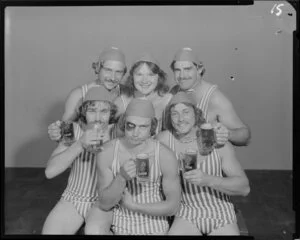 People (one with a fake black eye) in surf lifesaving costumes, drinking Lion beer in studio
