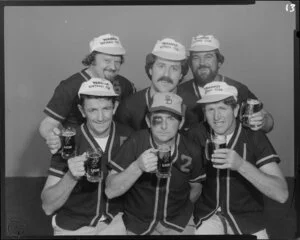 People (including one with fake black eye) in softball uniforms drinking Lion beer in studio