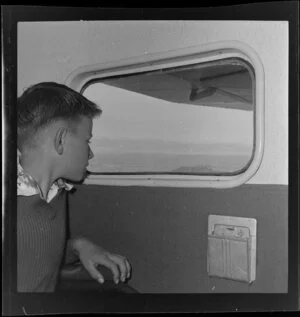 Unidentified boy passenger looking out of aeroplane window, Tourist Air Travel