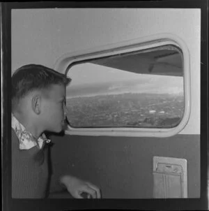 Unidentified boy passenger looking out of aeroplane window, Tourist Air Travel