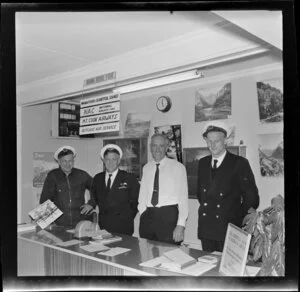 Lawson Burrows and Wilson Campbell with others at air services desk, Fiordland Travel, Te Anau