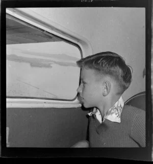 Unidentified boy passenger looking out aeroplane window, Tourist Air Travel