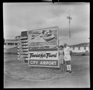 Fred and Mabel Ladd with Tourist Air Travel sign, Auckland Airport