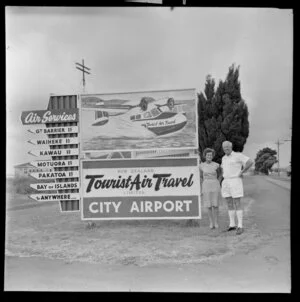 Fred and Mabel Ladd with Tourist Air Travel sign, Auckland Airport