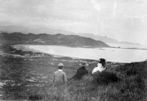 Three children, sitting on a hillside, looking over Lyall Bay, toward Moa Point
