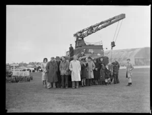 Group of people sheltering from rain with crane, Whenuapai airbase